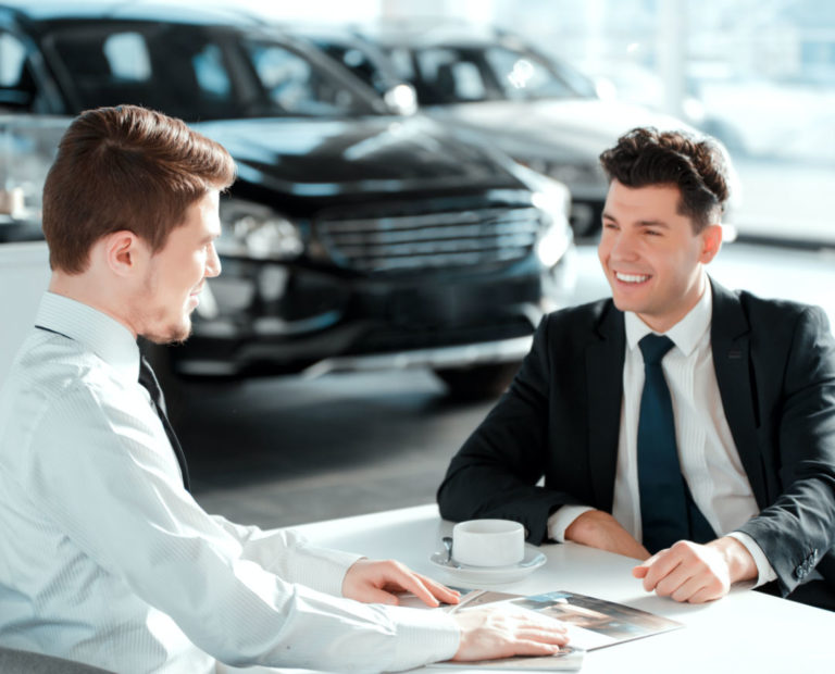 Two men sitting at a desk in front of each other in a car dealership
